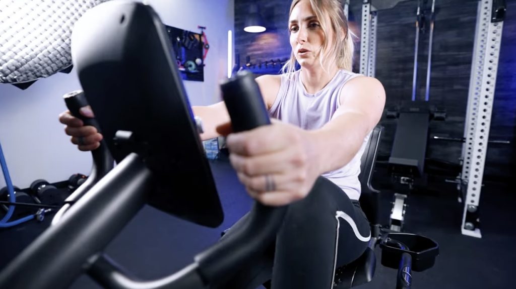 A woman is shown holding the handles while riding a Schwinn 230 Recumbent exercise bike