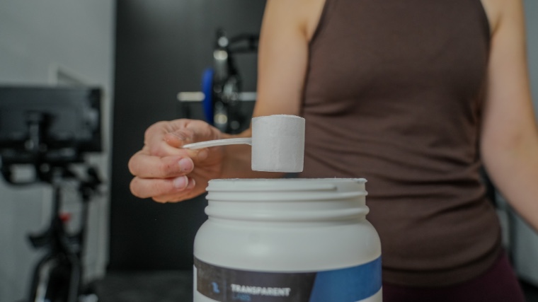 A person is shown lifting a scoop of Transparent Labs Bulk out of the container.